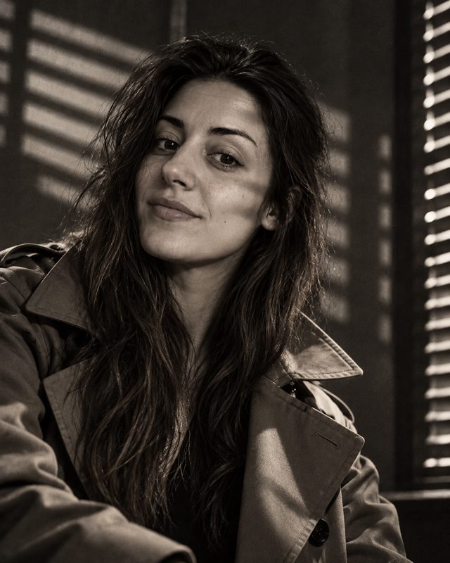 Example of the Film noir look: a black-and-white portrait of a woman in a trench coat, with light falling through blinds