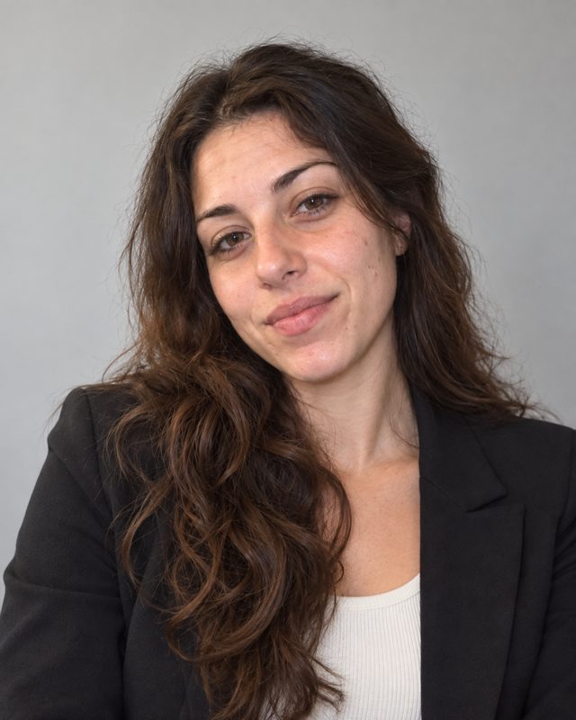 Example of the Professional profile look: a woman with long dark hair in a black blazer against a plain light-grey wall