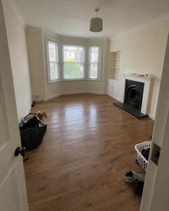 Example phone photo: an empty living room with a bay window, a fireplace and bags on the floor