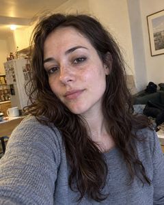 Example phone photo: a selfie of a woman with long dark hair in a grey top in her kitchen